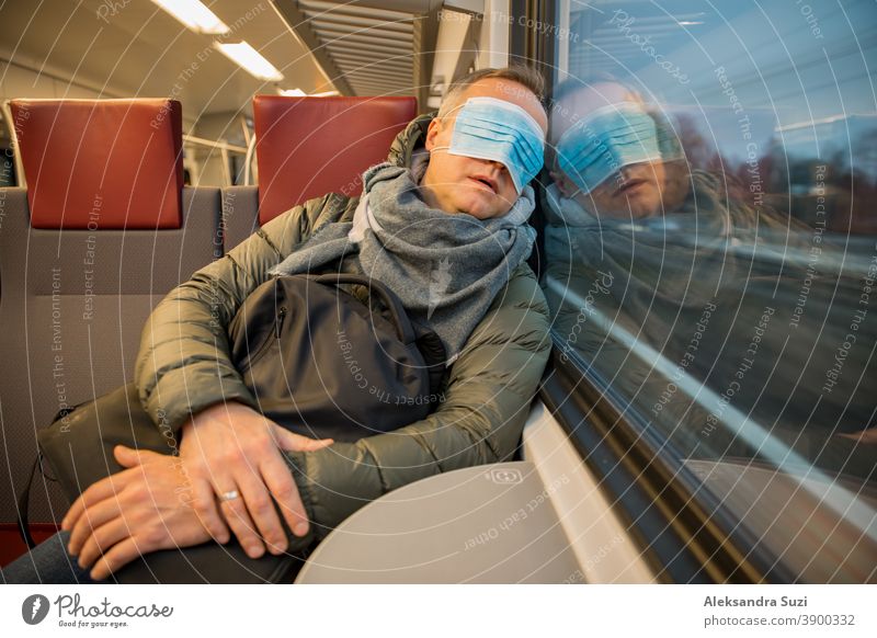 Traveling in public transport during the pandemic. Tired middle aged man wearing medical protective mask on his face sleeping in commuter train. city