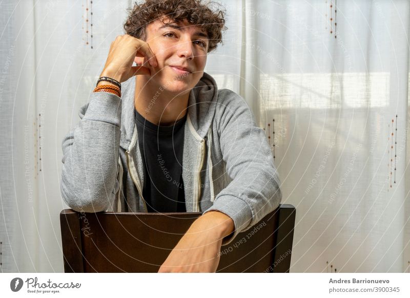 Attractive young man with curly hair wearing gray sweatshirt posing on white curtains background cheerful casual smile male adult handsome happy attractive