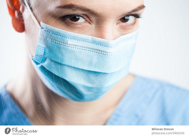 Young woman closeup detail headshot,wearing blue scrubs & protective face mask,attractive beautiful caucasian female doctor staring at camera,pretty eyes giving significant look,Coronavirus COVID-19