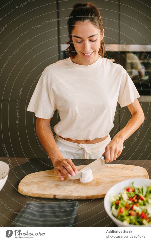 Smiling woman cutting cheese for salad in kitchen feta prepare cook vegetable delicious home female homemade knife healthy cutting board gourmet yummy culinary
