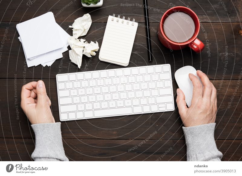 white wireless keyboard and mouse on a wooden brown table, next to a white cup with coffee business office computer workplace caucasian hand background notebook