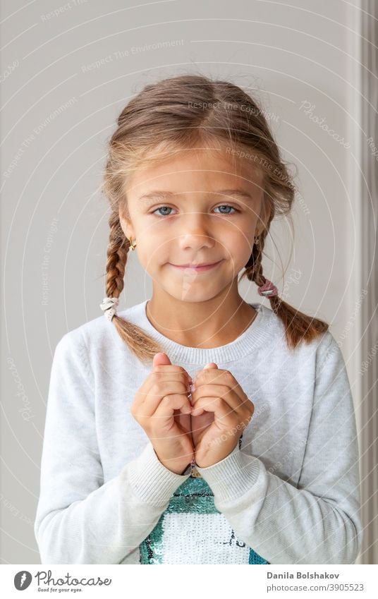 Portrait of cute little girl showing hand heart gesture, sweet precious child making body language, love, positive feeling and emotion adorable arms baby