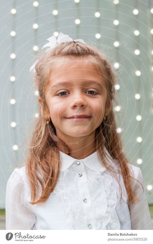 Portrait of cute charming little caucasian girl in white blouse and bow with background of glowing light bulbs people bright blur attractive shiny glitter