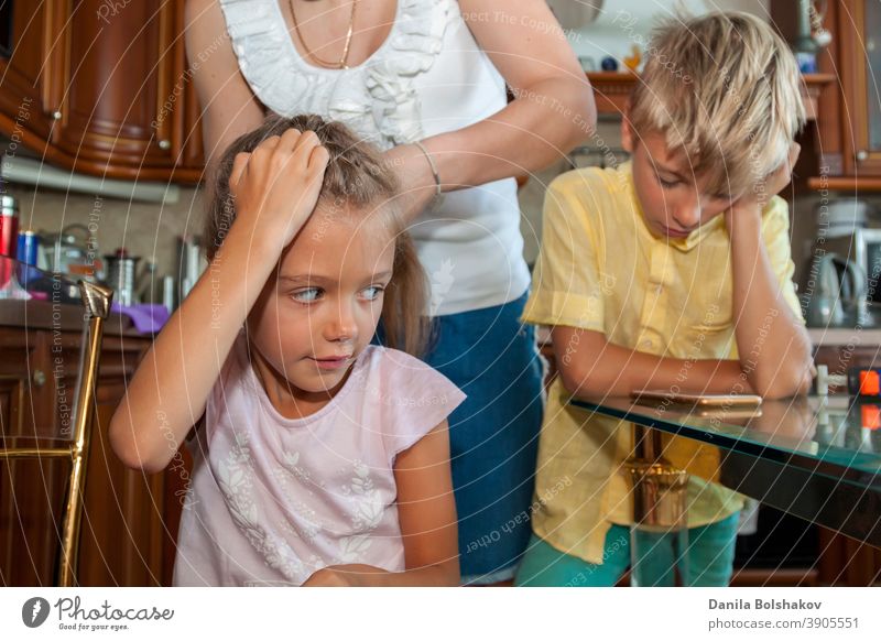 mother combs her daughter hair and braids it while boy in yellow shirt communicates via video link on mobile phone at home care caucasian cellphone child