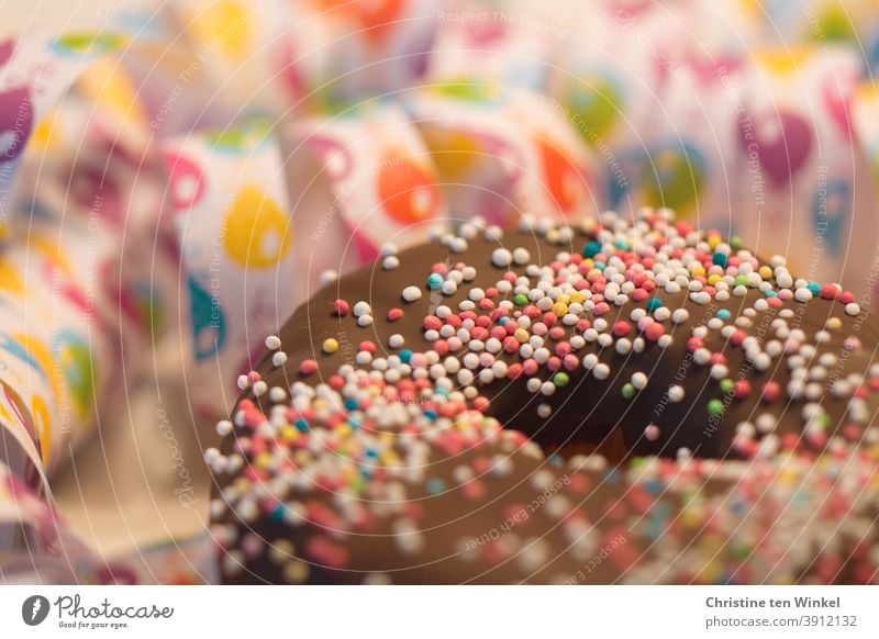 Donut / Doughnut with chocolate and sugar pearls. Behind them streamers with balloon motive in close-up. Weak depth of field with focus on the sugar beads