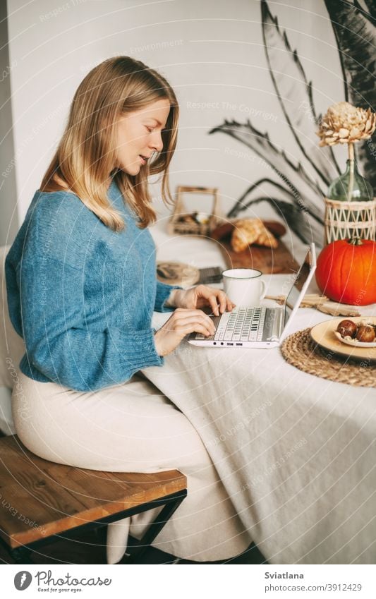 Cute blonde girl working in the morning on a laptop and drinking coffee. Work online, freelance, social distance using beautiful kitchen woman lifestyle