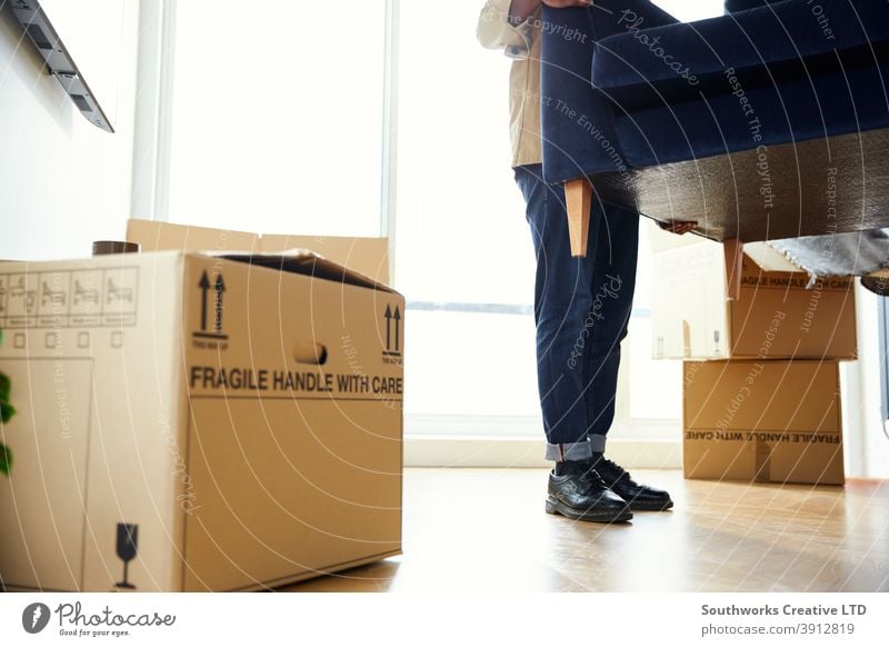 Close Up Of Man In New Home Carrying Sofa In Lounge On Moving Day Surrounded by Removal Boxes man young men house buying carrying lifting furniture sofa