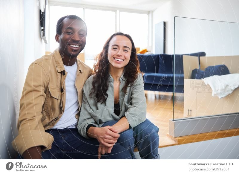 Portrait Of Young Couple Moving Into New Home Sitting On Floor In Lounge With Removal Boxes couple young couple house buying portrait looking at camera lounge