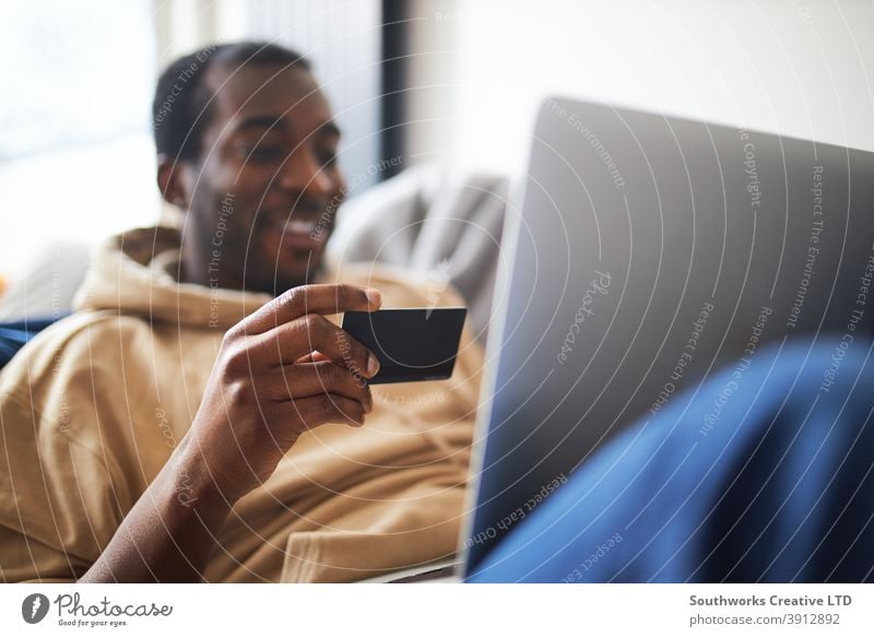 Young Man At Home Lying On Sofa With Laptop Using Credit Card To Shop Online man at home lying sofa lounge laptop computer credit card debit card pay day tech