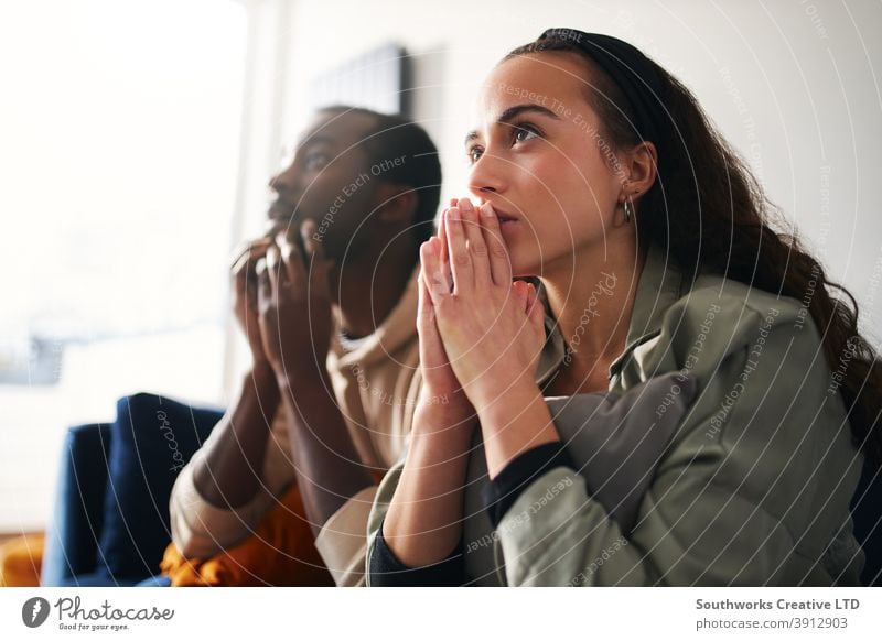 Excited Young Couple Relaxing At Home Sitting On Sofa Whilst Watching Sport On TV Together couple young couple at home sitting sofa lounge watching tv