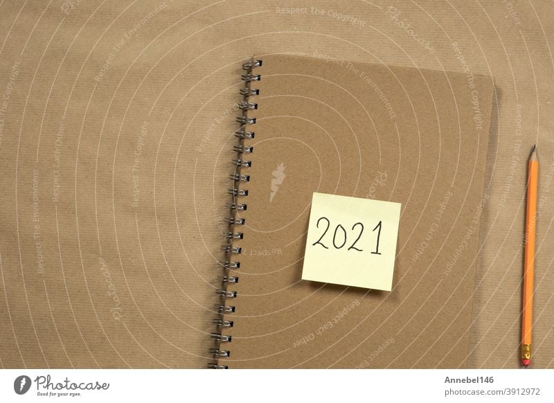 Top view of Brown notepad and yellow sticky note with 2021 new year message, pencil on brown paper background texture, education or business concept Clue Paper