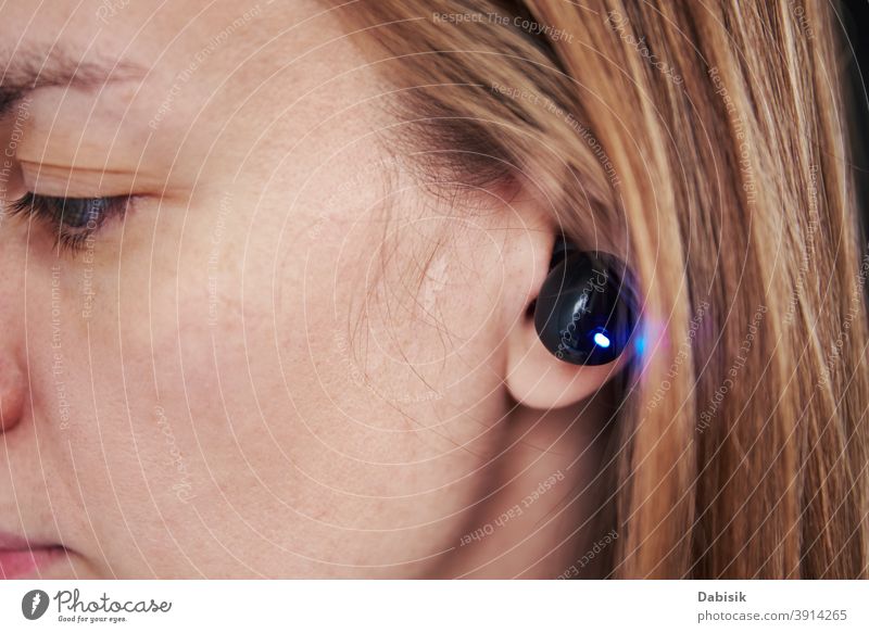 Woman listening music through wireless earphones. Caucasian woman using bluetooth headhones in the ear, close up audio black headphone equipment digital