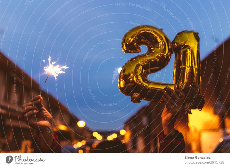 Celebrating with Gold foil balloons numeral 21 and sparkler at night. Happy New year 2021 celebration. numbers years sparkles congratulations glossy concepts