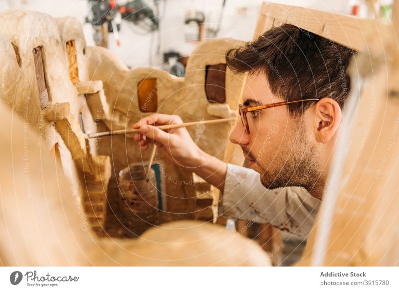 Craftsman making miniature model of clay house in studio workshop building artisan paint create male hobby facade professional skill craft concentrate talent