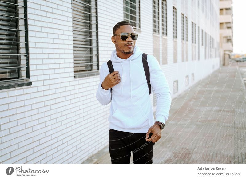 Stylish black man walking along street on sunny day - a Royalty