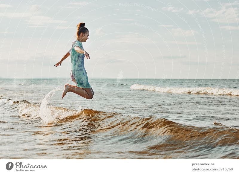 Girl enjoying sea jumping over waves spending a free time over sea on a beach during summer vacation excited positive sunset emotion carefree nature outdoors