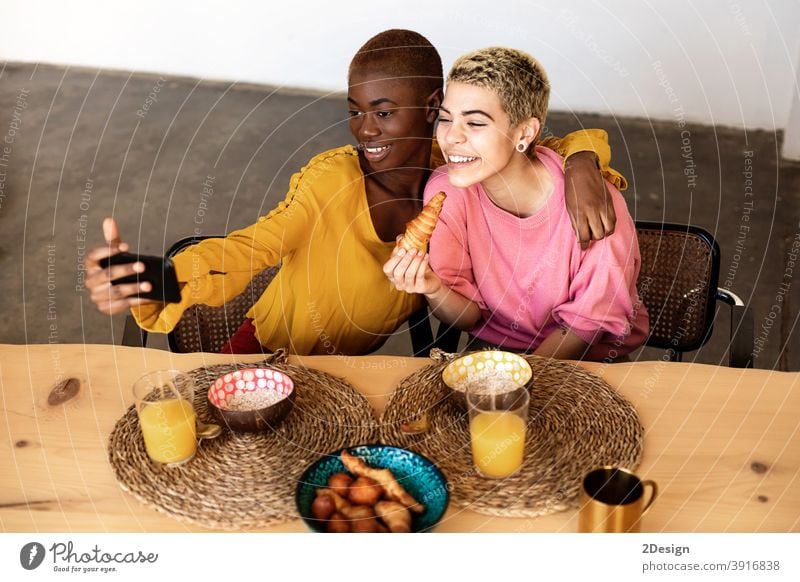 Beautiful young bestfriend females taking selfie using a smart phone and smiling while having a breakfast at home friendship domestic life together sitting