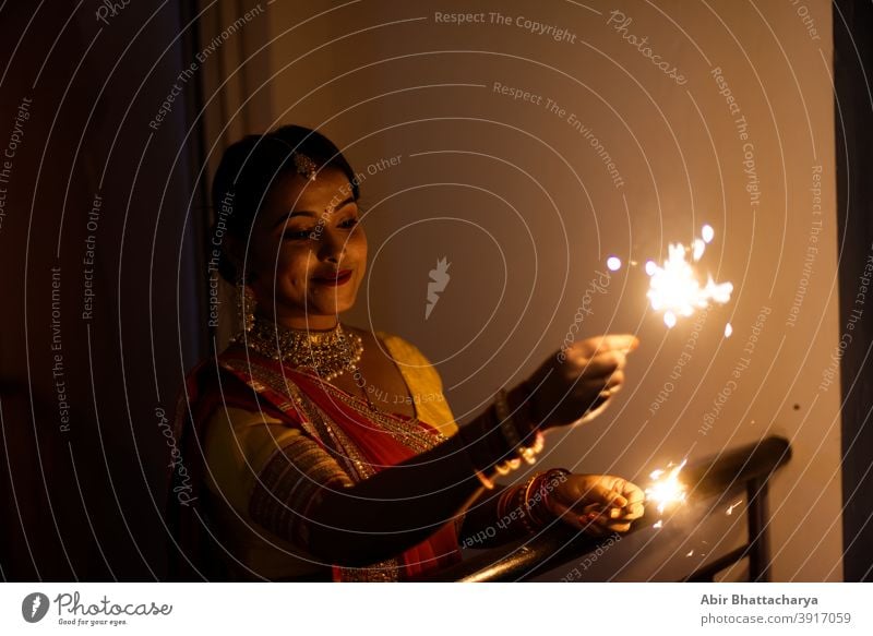 Young and beautiful Indian Bengali woman in Indian traditional dress is celebrating Diwali with fire crackers on a balcony in darkness. Indian lifestyle and Diwali celebration