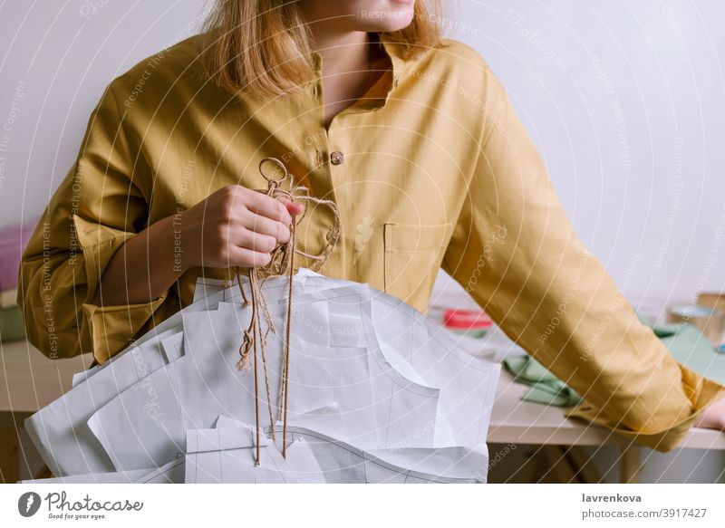 Female in yellow shirt holding paper dress patterns in her workshop tailor craft dressmaker fashion clothing occupation handmade faceless designer textile