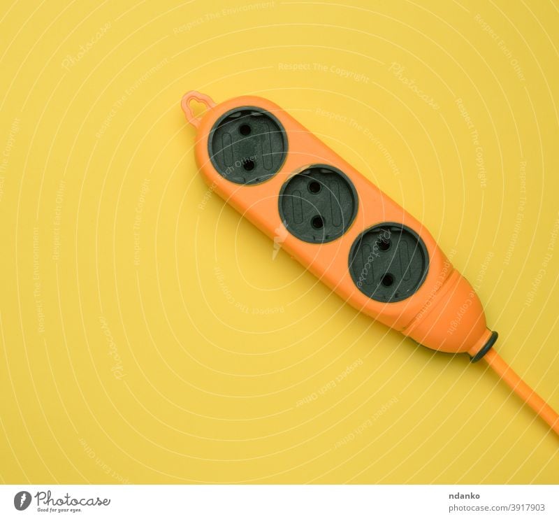rubber orange power strip with three sockets isolated on a yellow background supply tool wire adapter cable closeup connection cord device electric electrical