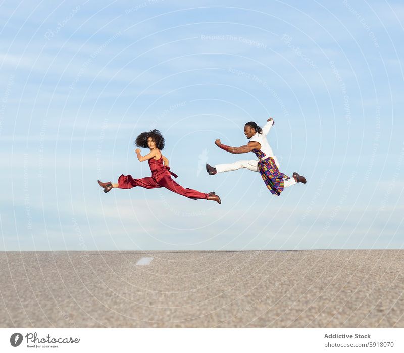 Acrobatic couple jumping above road in summer dance acrobatic trendy fancy perform dancer energy style african american ethnic black asphalt together leap
