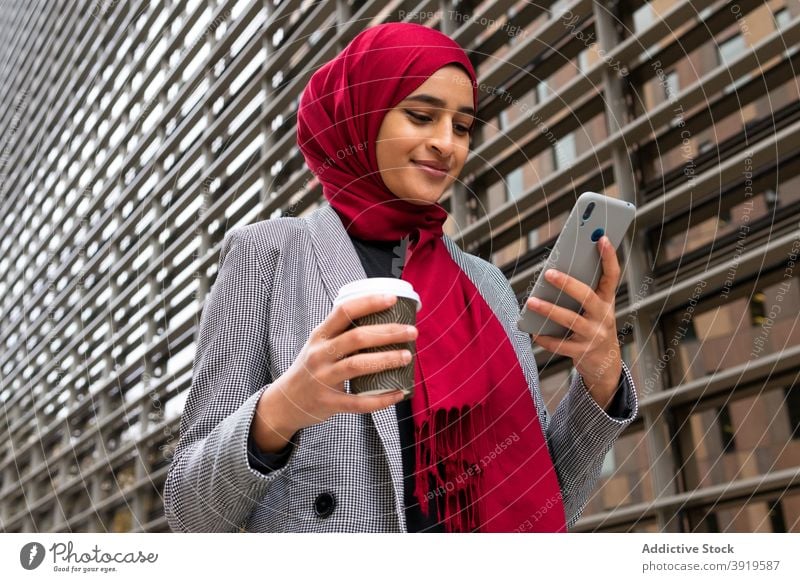 Happy ethnic woman in hijab browsing smartphone on street tradition muslim takeaway coffee message city female arab social media using gadget surfing internet