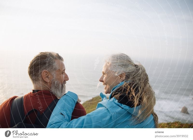 caucasian senior couple sitting on cliff enjoying sunset together looking at each other woman happy old elderly love smiling people family mature retirement
