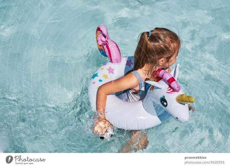 Little girl playing in a swimming pool with inflatable ring toy in the shape of unicorn authentic backyard childhood family fun happiness happy joy kid