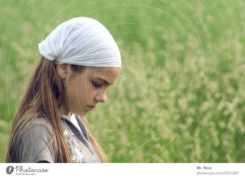 Young girl with headgear looks to the ground Girl Hair and hairstyles Upper body Fashion Nature Headscarf Face Youth (Young adults) Headwear Landscape Meadow