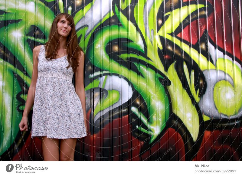 Young woman stands in front of a graffiti wall and looks shyly to the left Summer dress Wall (building) Art Characters Street art Facade Woman Long-haired