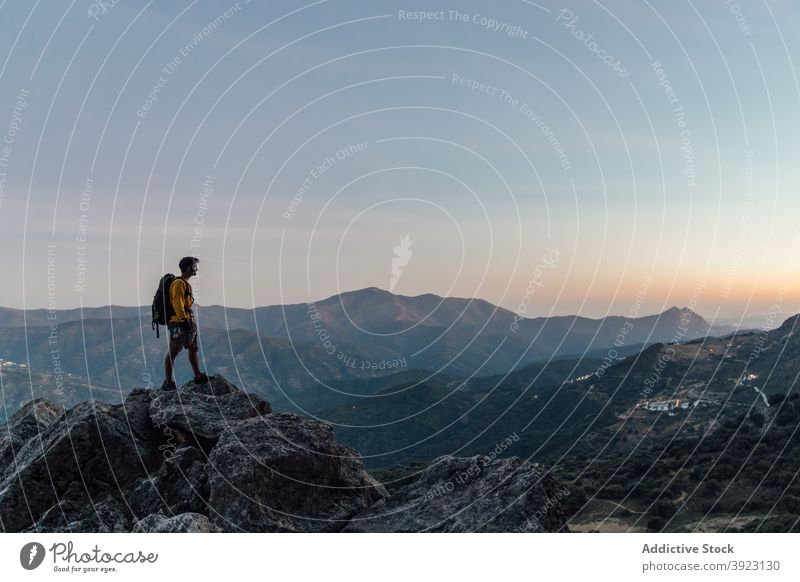 Traveling man standing on rocky summit at sunset traveler mountain freedom lonely explorer rough adventure backpack top nature male wanderlust hike highland