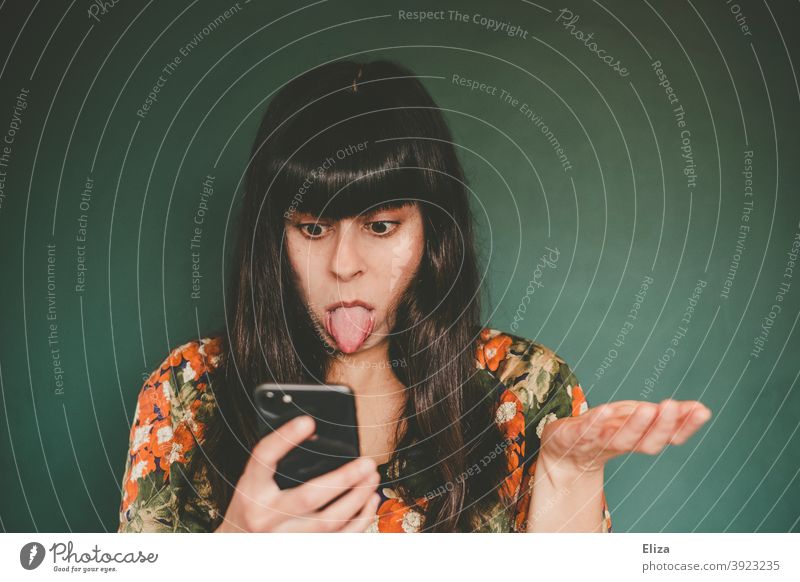 Young woman sticks her tongue out at her cell phone annoyed Cellphone Exasperated smartphone Woman Tongue frustrated impatiently Stick out Face