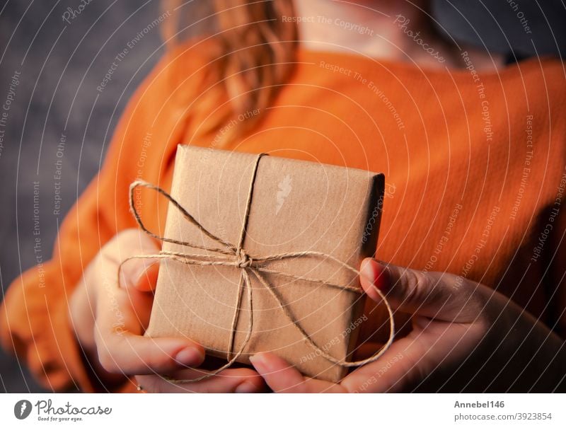 Young Female holding a kraft gift box, wrapped in plain brown paper, Valentines day, Birthday, Mothers Day present or gift concept selective focus, dark background