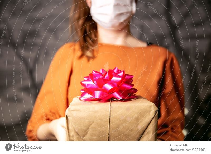 Young Female holding a kraft paper gift box with pink decoration with medical protective face mask for Coronavirus, Covid-19 and present concept. Birthday or Valentines day retro design