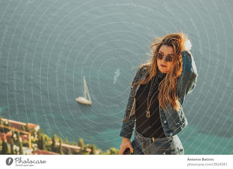 Portrait of an attractive brunette with sunglasses posing sensually with the bright blue adriatic sea behind her. Small sailboat on the sea near Dubrovnik, concepts of travel with copyspace room