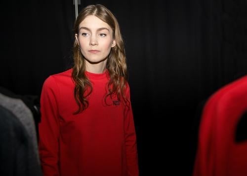 A short break during a photo shoot in a backstage where models are getting ready. A beautiful brunette girl is preparing for a model test while wearing a comfy red sweater.