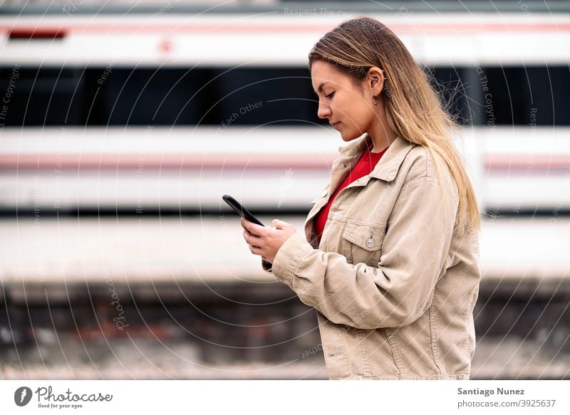 Blonde Girl Waiting For Train side view woman caucasian train motion portrait using phone typing looking background standing female outside outdoors metro