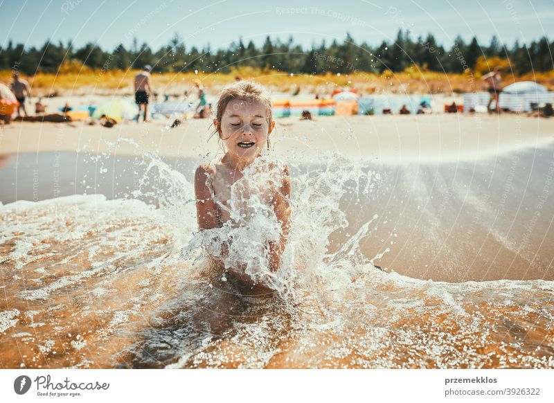 Little girl splashed by sea wave while sitting and playing on a beach recreation cute outdoors positive sunlight summertime family enjoy joyful seaside ocean