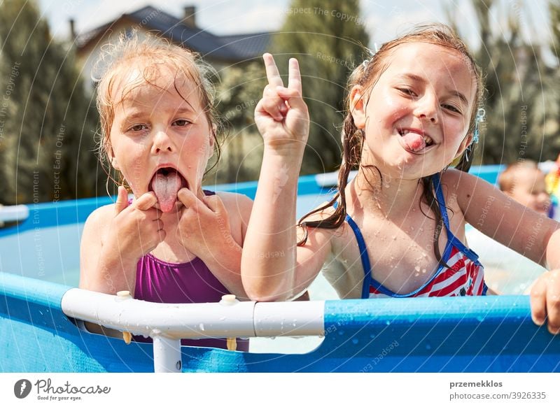 Happy girls making V sign gesture silly face playing in a pool authentic backyard childhood children family fun garden happiness happy joy kid laughing