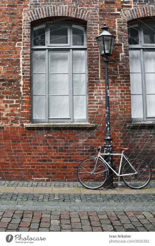 White bicycle tied to a streetlamp in front of a brick wall bike background retro vintage laterne architecture europe european facade germany house outdoor