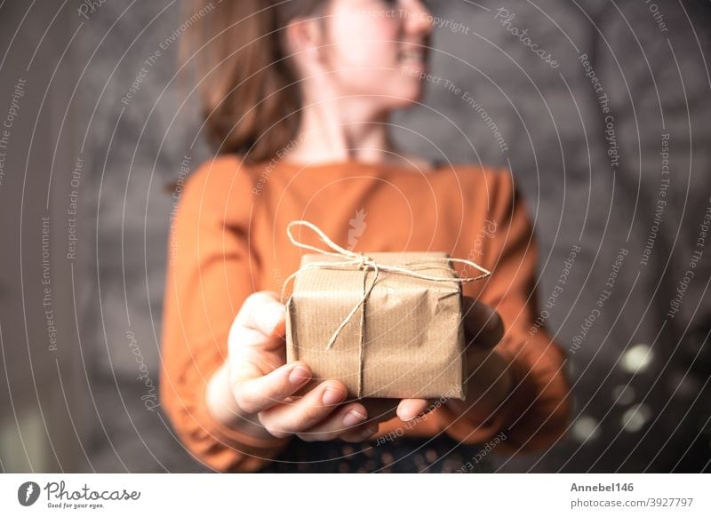 Young female holding a small craft paper gift box, plain brown paper for recycle and present. Birthday, Valentines concept christmas package ribbon holiday