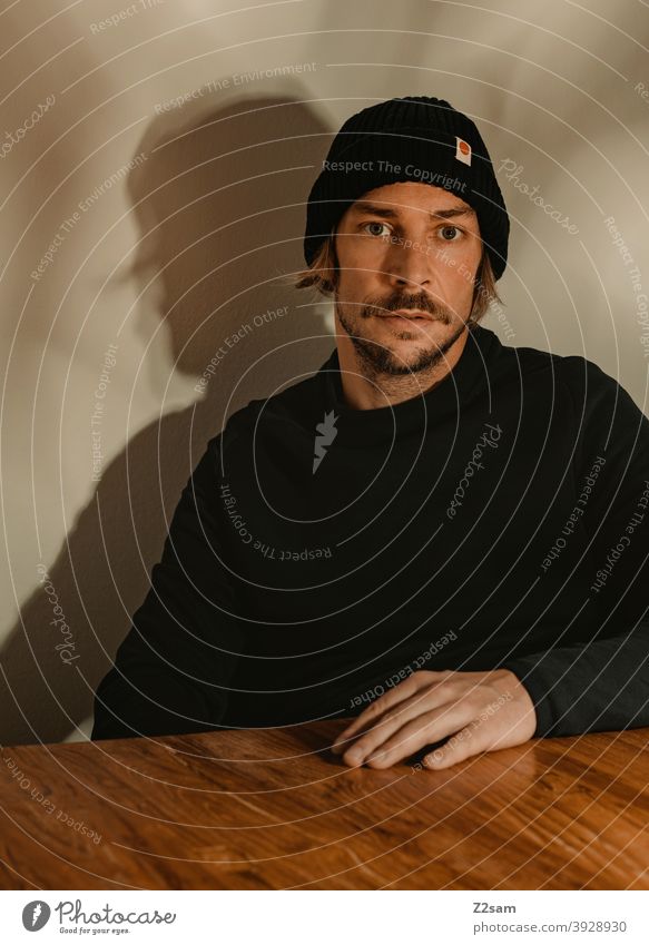 Portrait of a young man portrait Young man Cap Sweater honestly atmospherically Wooden table Facial hair Moustache sincerely Modern fashionable naturally