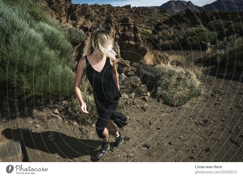 A lost girl is running through the rough terrain of the heart of Tenerife - Teide volcano fields. Blondie dressed in a black dress is in a hurry though this moody landscape seems to be empty after all. Only rocks, stones, and mountains.
