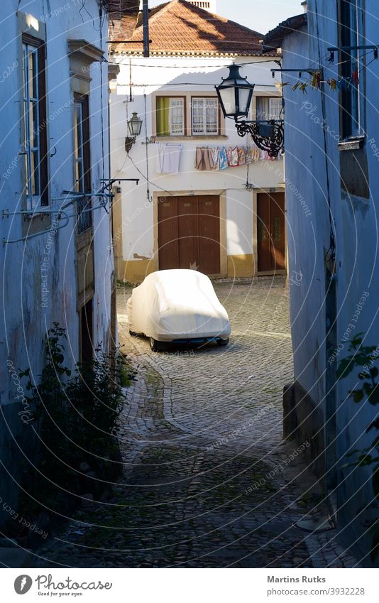 Anonymous car under cover on a narrow cobbled street. anonymous empty tarp tarpaulin old cobblestone white houses laundry line lanterns travel alone Off-Season