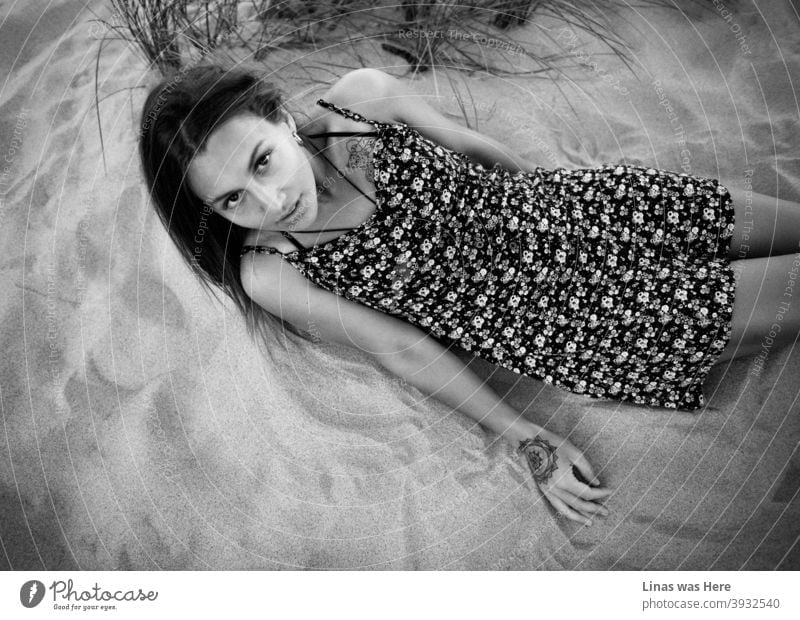 A wonderful brunette model dressed in a light dress is lying on the sand. Even though the image is black & white, it is obvious that she is perfectly tanned while enjoying the summer sun. Her big black eyes are staring right into the camera.