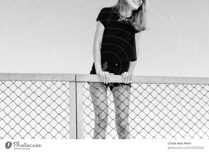 Happy girl is climbing a fence on a perfect summer day. Big smile, long legs, and black outfit. A throwback to warmer and happier days. black and white happy