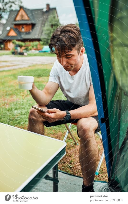 Young man drinking a coffee sitting at front of tent in the morning adventure beverage break breakfast camp camping closeup cup exploration freedom hiker hot