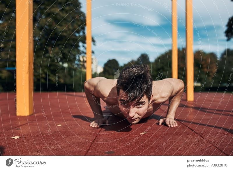 Young shirtless man bodybuilder doing push-ups on a red rubber ground during his workout in a modern calisthenics park care caucasian health lifestyle male one