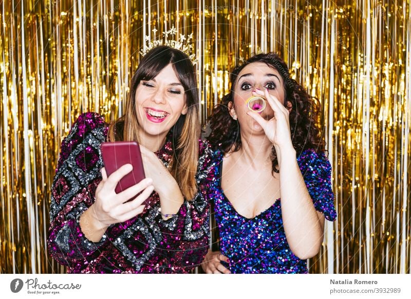 Two beautiful women with party clothes and Christmas headbands having fun together in a New Year's Eve party with some portraits of them. New Year's Eve concept