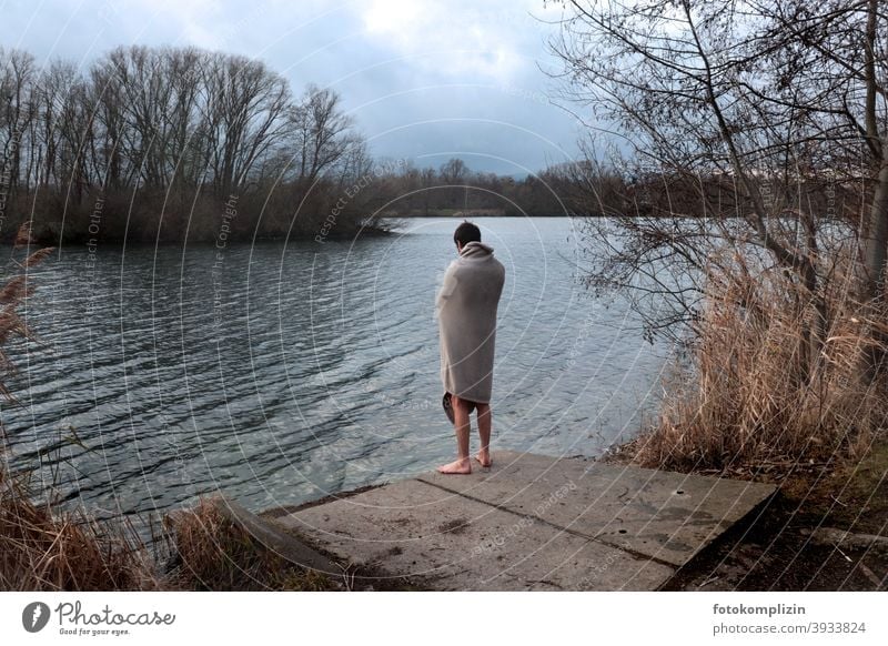 Young man wrapped naked in blanket in winter, looking at a lake Ice Swimming Winter Bathing Ice bathing salubriously Winter's day bathe chill Rear view
